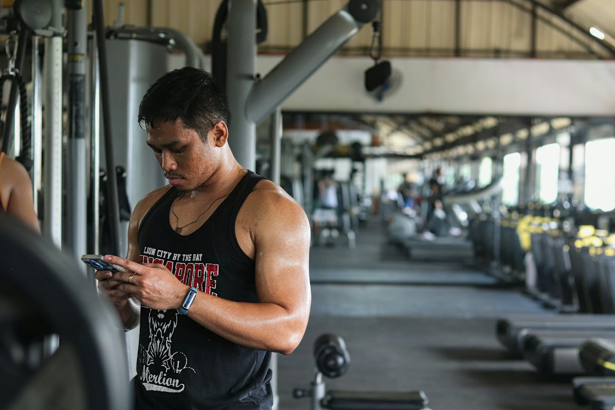 Homem de regata olhando o celular entre os aparelhos de uma academia